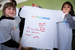Foto di due bambine che mostrano una maglietta firmata da John Elkann e dal sindaco di Torino Stefano Lo Russo.