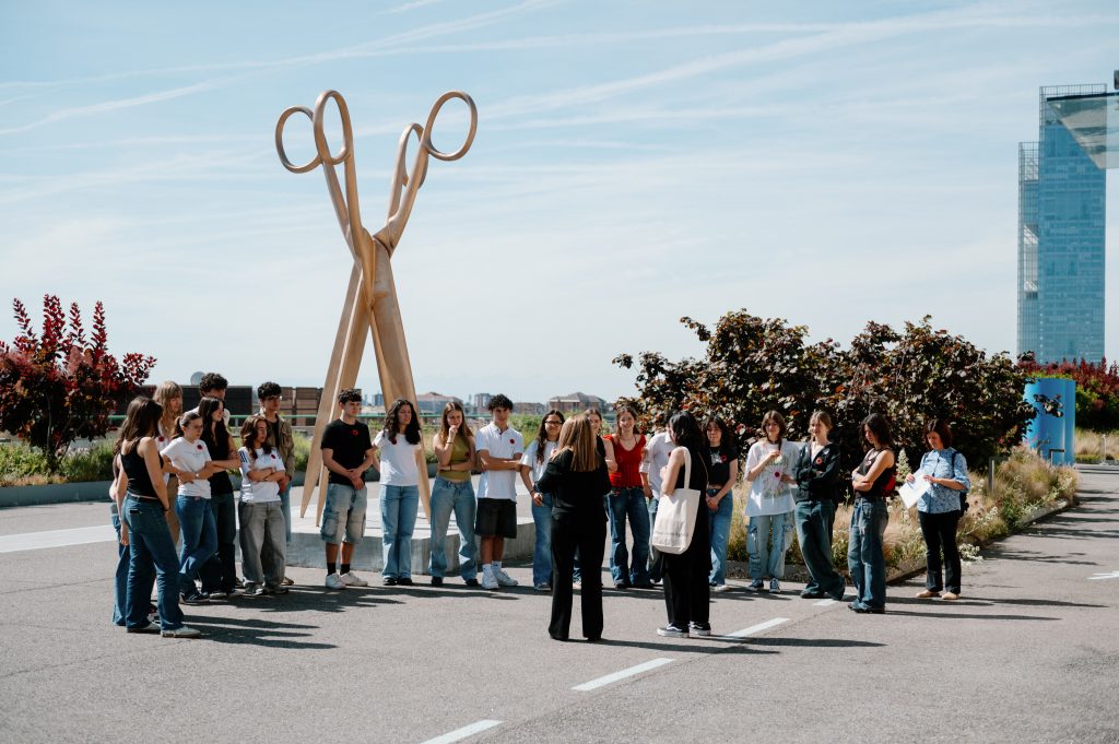 Foto di una classe di studenti e studentesse sulla Pista 500 che ascolta una mediatrice della Pinacoteca che spiega un'opera d'arte